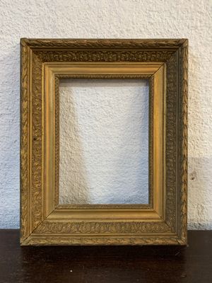 an old picture frame sitting on a table against a white wall