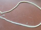 un collier de perles blanches muni d'un fermoir en argent, posé sur une table