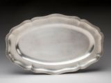 a silver plate with a scalloped edge on a gray surface