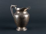an antique silver pitcher on a black background with a gray background