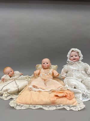 trois poupées représentant des bébés sont assises sur une couverture posée sur une surface grise