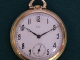 une montre de poche en or avec un cadran blanc, posée sur un tissu vert