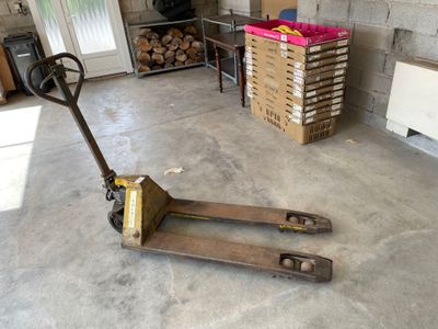 a fork lifter in a garage with a pile of wood in the background