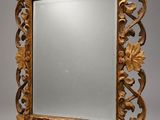 an ornately carved mirror with leaves and scrolls on a gray background
