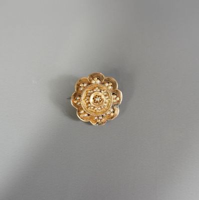une image représentant une broche en forme de fleur dorée posée sur une surface grise