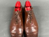 pair of brown leather shoes with red soles on a grey surface