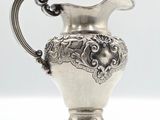 an antique silver plated pitcher on a white surface with a white background