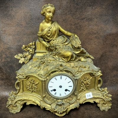 a gold clock with a woman sitting on top of it