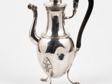 a silver tea pot with a black handle on a stand