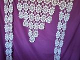 purple and white crocheted shawl hanging on a purple curtain