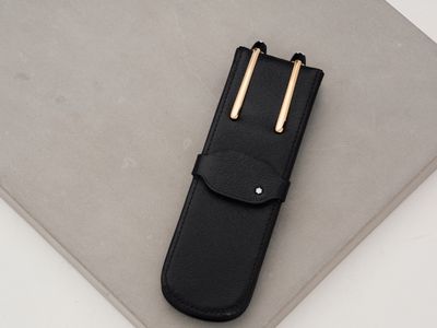 black leather pen case with two gold pins on top of a white surface