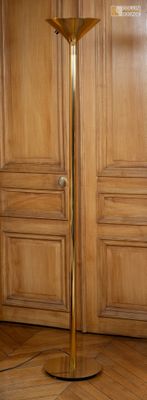un lampadaire doré posé sur un parquet, devant une porte en bois