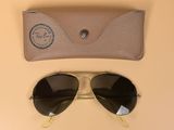 une paire de lunettes de soleil et son étui posés sur une table, sur fond beige