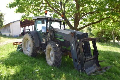 a tractor that is parked in the grass near a tree
