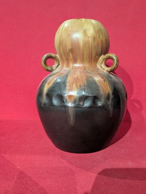 a black vase with a wooden handle on a red surface
