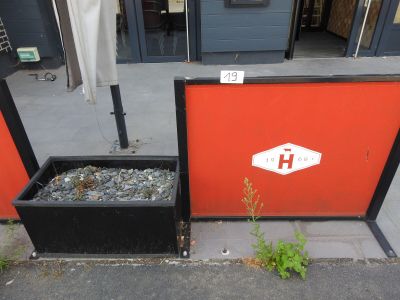 un mur rouge sur lequel sont posés une jardinière noire et une pancarte