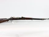un vieux fusil repose sur une surface blanche, à côté d'une bouteille en verre