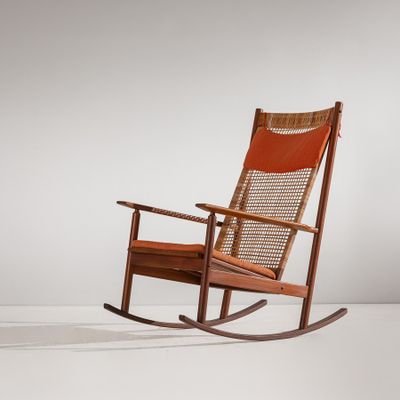 Le fauteuil à bascule est en bois et son assise est en cuir orange.