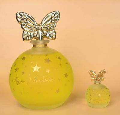 un flacon de parfum orné d'un papillon sur le bouchon, à côté d'un petit flacon de parfum