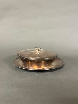 un plat en argent muni d'un couvercle, posé sur une surface grise