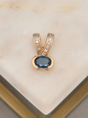 une photo d'un pendentif en saphir bleu et diamants posé sur une surface en marbre blanc