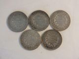 six different coins are arranged in a row on a white surface
