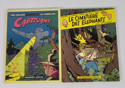 Deux bandes dessinées sont posées sur une table devant un mur blanc.