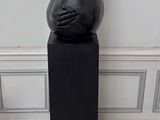 une sculpture noire représentant un ours assis sur un socle noir