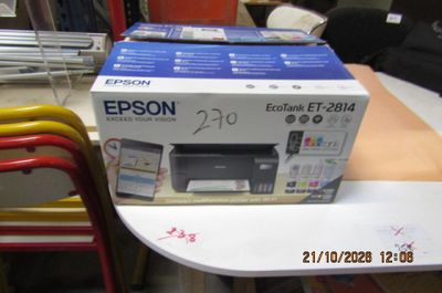 un carton contenant une imprimante posé sur une table à côté d'une pile de chaises