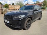 the bmw x5 is parked in a parking lot in front of a pile of logs