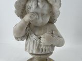une statue représentant une petite fille coiffée d'un chapeau, posée sur un socle