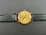 a gold watch on a black strap on a gray surface