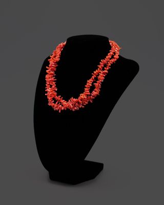 un collier composé de perles de corail, présenté sur un mannequin noir