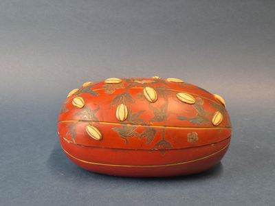 une boîte rouge ornée de motifs dorés, posée sur un fond gris