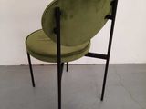 a green chair sitting on top of a cement floor next to a white wall