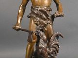 une statue antique en bronze représentant un homme avec un coq, posée sur un socle
