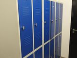 Plusieurs casiers bleus sont alignés dans un couloir, à côté d'une porte noire.