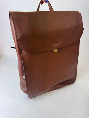 brown leather backpack on a white background with a red and blue ribbon