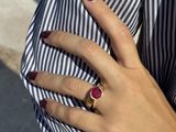 woman ' s hand holding a ring with a red stone on it