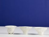 three white bowls sitting on top of a white table next to a blue wall