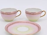 two pink and gold cups and saucers on a white surface