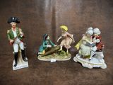three figurines of people sitting on top of a brown surface
