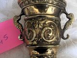 a brass vase with a handle on a lace tablecloth