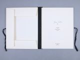 a white book with a black ribbon is open on a gray surface