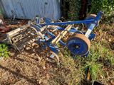 une charrue bleue posée dans l'herbe à côté d'un bâtiment