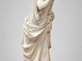 une statue en marbre blanc représentant une femme, la main posée sur le menton
