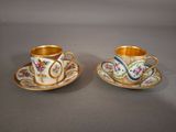 two cups and saucers with floral designs on them on a table