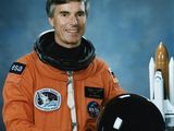 une image représentant un homme vêtu d'une combinaison spatiale orange et tenant un casque