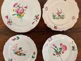 four white plates with pink flowers on them sitting on a wooden table