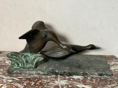 une statue en bronze représentant un canard, posée sur un socle en marbre